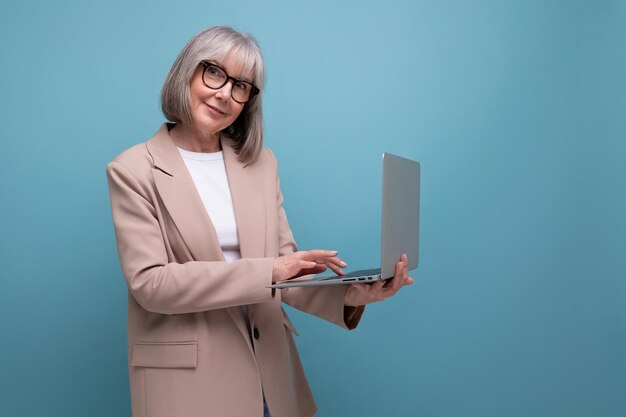 Mujer adulta confiada en una chaqueta con una computadora portátil en un fondo brillante con espacio para copiar