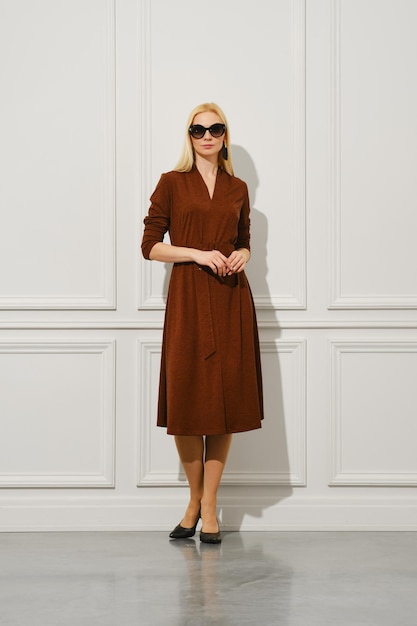 Una mujer adulta se para con confianza en el interior con un elegante vestido marrón