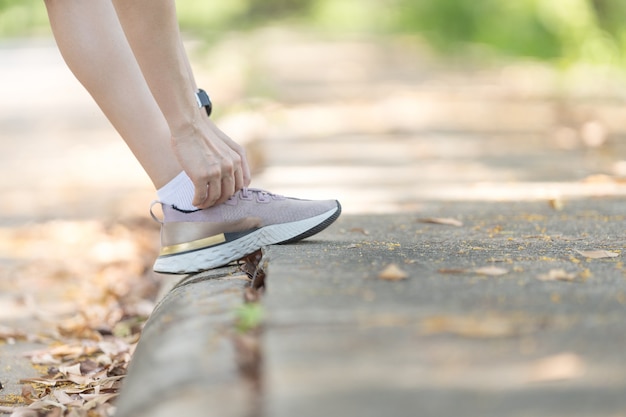 Mujer adulta corredor atar cordones de los zapatos para hacer ejercicio en el parque de la ciudad