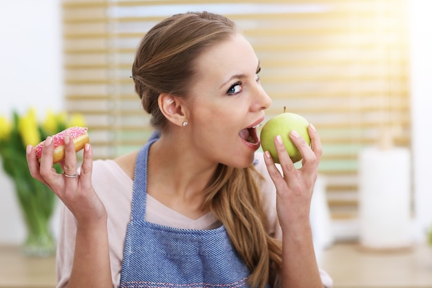 Mujer adulta eligiendo entre bocadillos saludables y no saludables en la cocina