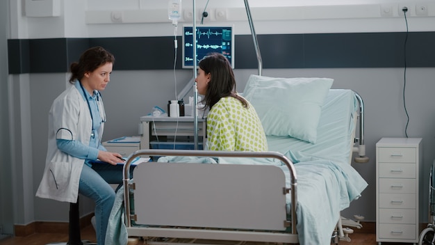 Mujer adulta enferma sentada en la cama mientras el médico examina la enfermedad