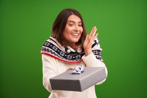 Mujer adulta feliz con regalo de Navidad sobre fondo verde