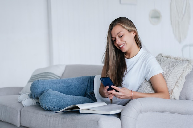 Mujer adulta joven caucásica pensativa en jeans azules y camiseta blanca sostiene que el teléfono lee inesperado