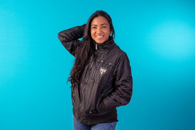 Mujer adulta joven en chaqueta de nailon negro en foto de estudio con fondo azul.