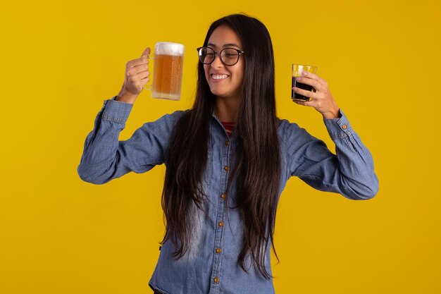 Mujer adulta joven en fotos de estudio haciendo expresiones faciales y sosteniendo un vaso de cerveza y una taza de café