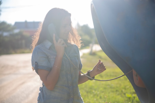 Mujer adulta joven hablando por un teléfono público en la calle en una aldea rusa bajo el sol