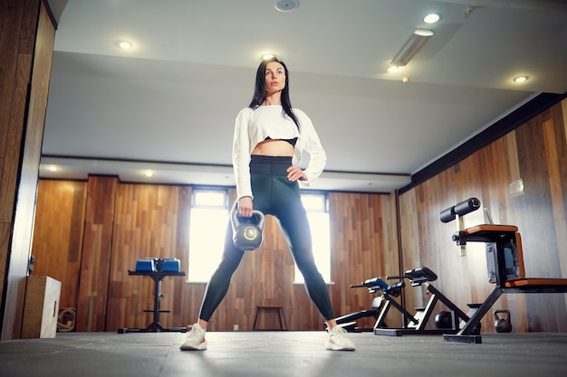 Mujer adulta joven haciendo ejercicios de swing con pesas rusas como parte de un entrenamiento físico