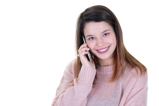 Mujer adulta joven hermosa que habla en el teléfono móvil que se coloca cerca de la pared del fondo y del espacio blancos de la copia