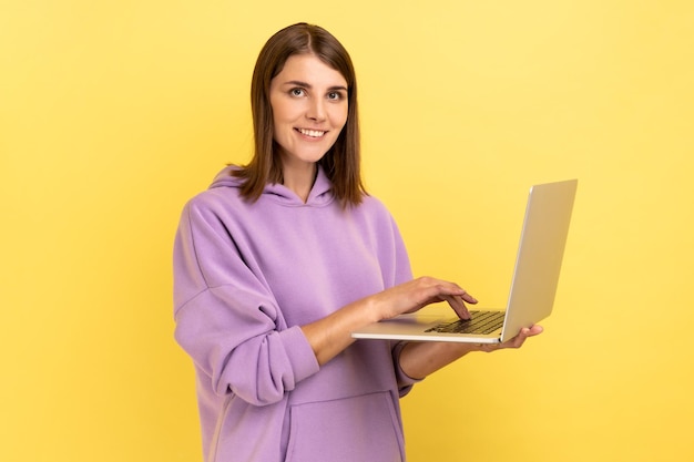 Mujer adulta joven optimista que trabaja en computación portátil mirando a la cámara con cara feliz