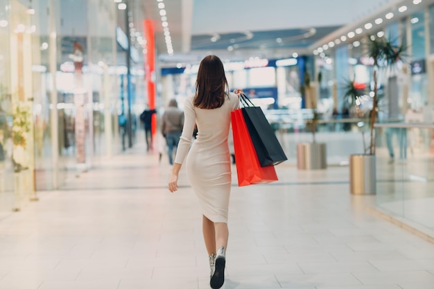 Mujer adulta joven positiva que lleva bolsas de papel en las manos Vista trasera trasera