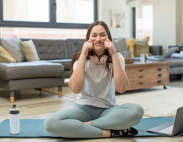 Foto mujer adulta joven practicando yoga sonriendo y apuntando a su propia sonrisa falsa