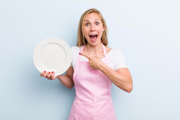 Mujer adulta joven rubia sosteniendo un concepto de chef de plato vacío