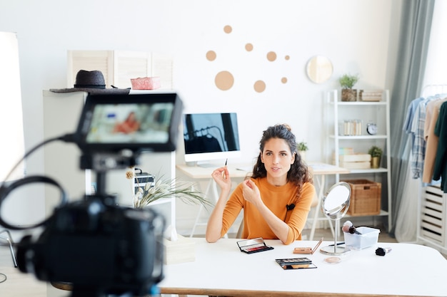 Mujer adulta joven sentada sola en su habitación grabando un nuevo video para su canal de blog de belleza