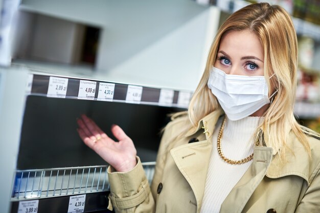 Foto mujer adulta en máscara médica delante de los estantes vacíos en la tienda de comestibles