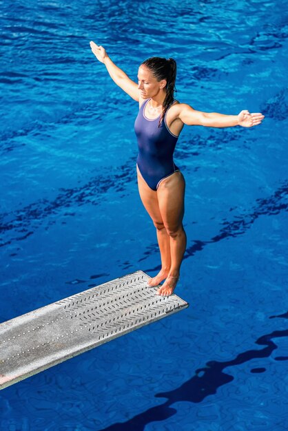 Mujer adulta media con los brazos extendidos de pie en una plataforma de buceo