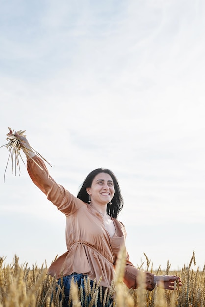 Mujer adulta media en camisa beige de pie en un campo de trigo con amanecer en la vista trasera de fondo