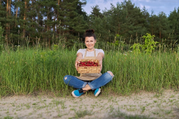 Mujer adulta media con cesta de fresas frescas arrancadas en el campo, alimentos orgánicos saludables