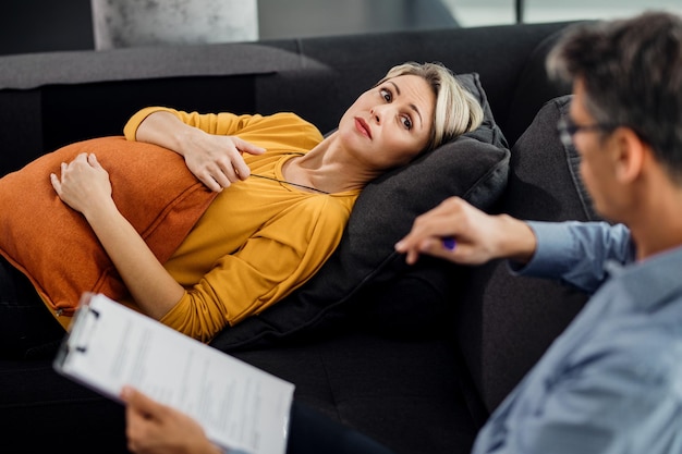 Mujer adulta media escuchando a su terapeuta mientras está acostada en el sofá del psiquiatra