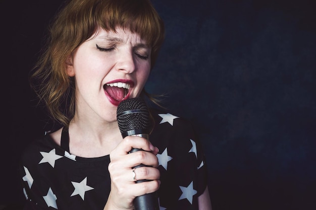 Mujer adulta media con los ojos cerrados cantando mientras está de pie contra un fondo negro