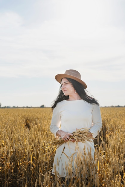 Mujer adulta media con vestido blanco de pie en un campo de trigo con amanecer en la vista trasera de fondo