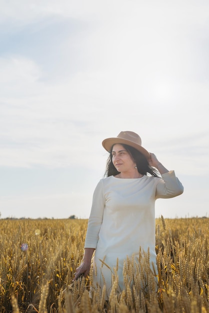 Mujer adulta media con vestido blanco de pie en un campo de trigo con amanecer en la vista trasera de fondo