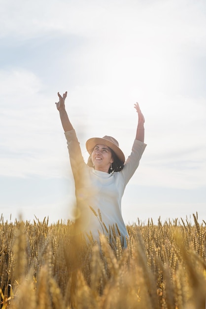 Mujer adulta media con vestido blanco de pie en un campo de trigo con amanecer en la vista trasera de fondo