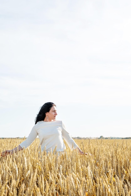 Mujer adulta media con vestido blanco de pie en un campo de trigo con amanecer en la vista trasera de fondo