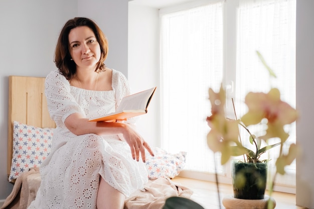 Mujer adulta de mediana edad leyendo un libro junto a la ventana