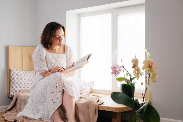 Mujer adulta de mediana edad plus size leyendo un libro junto a la ventana