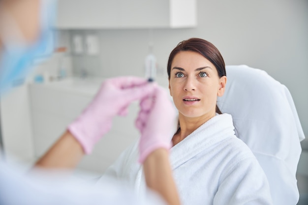 Mujer adulta mirando con ojos saltones a un médico en guantes de látex con una jeringa delante de ella