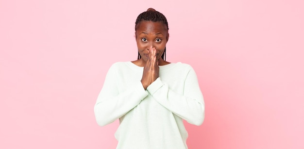 Mujer adulta negra afro feliz y emocionada, sorprendida y asombrada cubriendo la boca con las manos, riendo con una expresión linda