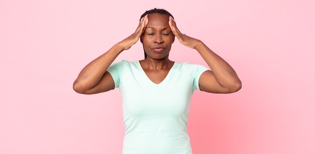 Mujer adulta negra afro que parece concentrada, pensativa e inspirada, intercambiando ideas e imaginando con las manos en la frente