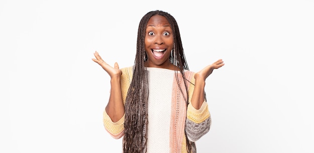 Mujer adulta negra afro que parece feliz y emocionada, sorprendida con una sorpresa inesperada con ambas manos abiertas junto a la cara