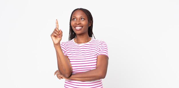 Mujer adulta negra afro sonriendo felizmente y mirando hacia los lados, preguntándose, pensando o teniendo una idea