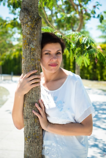 Una mujer adulta en el parque abrazando a un árbol y sonríe