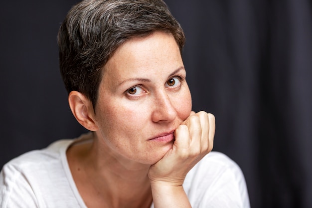 Mujer adulta pensativa con el pelo corto. Retrato sobre un fondo negro.