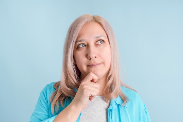 Una mujer adulta piensa con la mano debajo de la barbilla. Retrato de primer plano sobre un fondo azul.