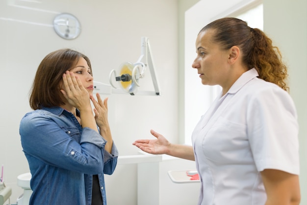 Mujer adulta que sufre de dolor de muelas y se queja durante la visita al dentista profesional
