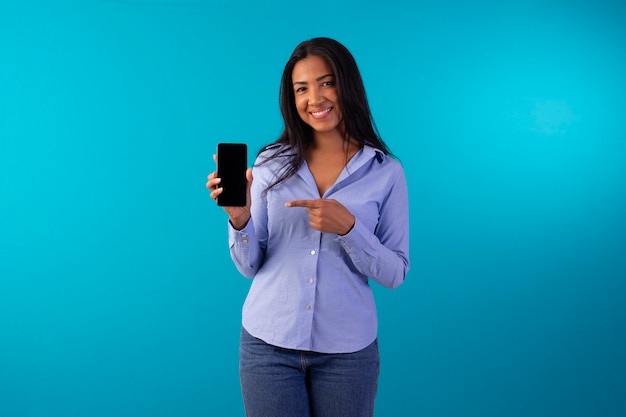 Mujer adulta en ropa formal, vestida con camisa azul y jeans en foto de estudio con fondo azul.