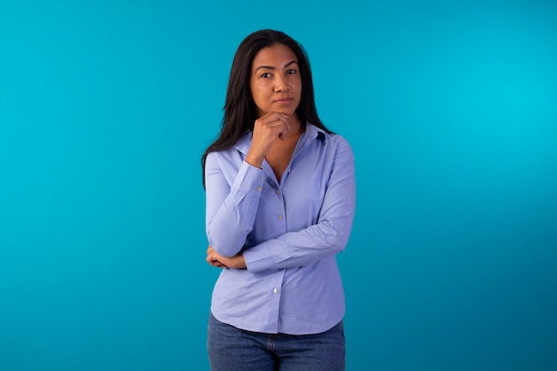 Mujer adulta en ropa formal, vestida con camisa azul y jeans en foto de estudio con fondo azul.