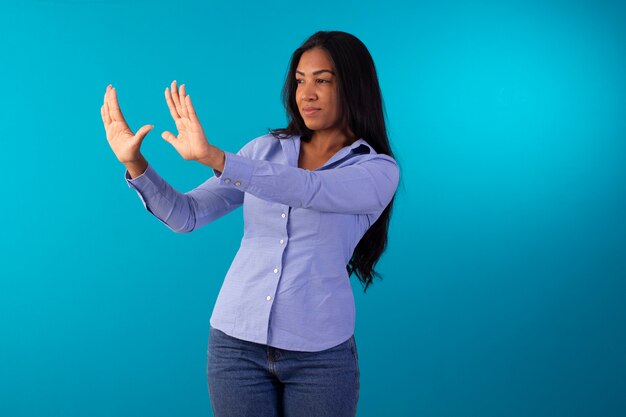 Mujer adulta en ropa formal, vestida con camisa azul y jeans en foto de estudio con fondo azul.