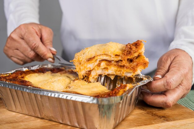 Una mujer adulta sacando una porción de lasaña recién hecha con boloñesa lista para comer