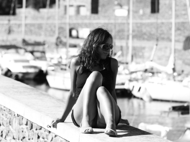 Mujer adulta sentada en una pared de retención en el puerto durante un día soleado