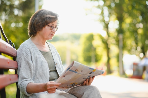 Mujer adulta sentada en el parque y leyendo periódicos