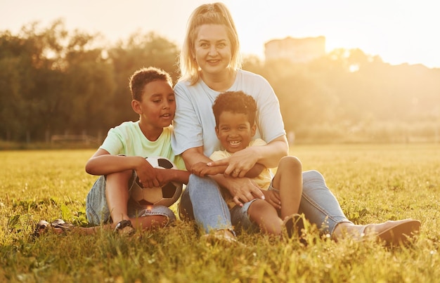 La mujer adulta se sienta con dos niños negros en el campo durante el día de verano
