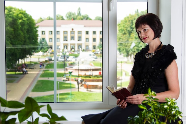 Una mujer adulta se sienta junto a la ventana y lee un libro Una mujer en la biblioteca