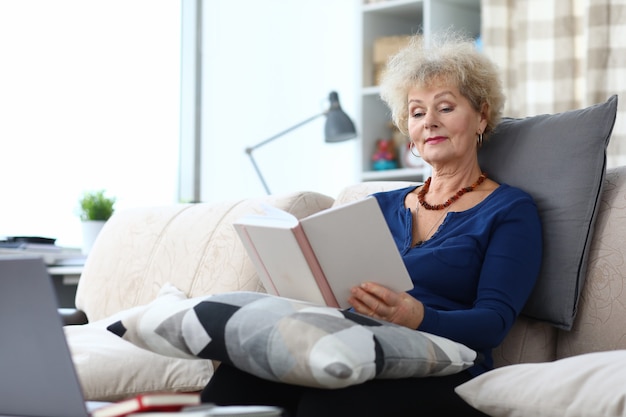 Mujer adulta se sienta en el sofá en casa y lee el libro.