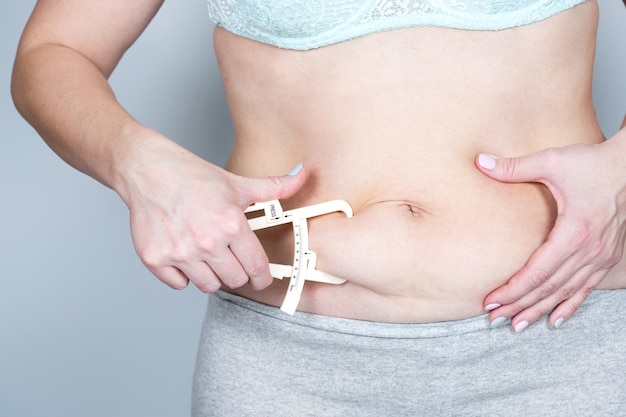 La mujer adulta con sobrepeso o grasa mide el pliegue graso del abdomen con un calibre. Concepto de estilo de vida saludable y adelgazante