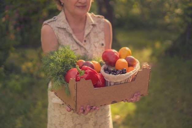 Mujer adulta sosteniendo una caja con nueva cosecha de temporada fresca en el jardín