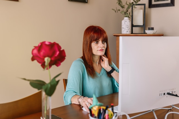 Mujer adulta teletrabajando con una computadora en casa en un escritorio con un despertador